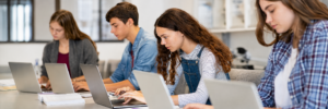 High school students independently completing online tests on laptops in a classroom.